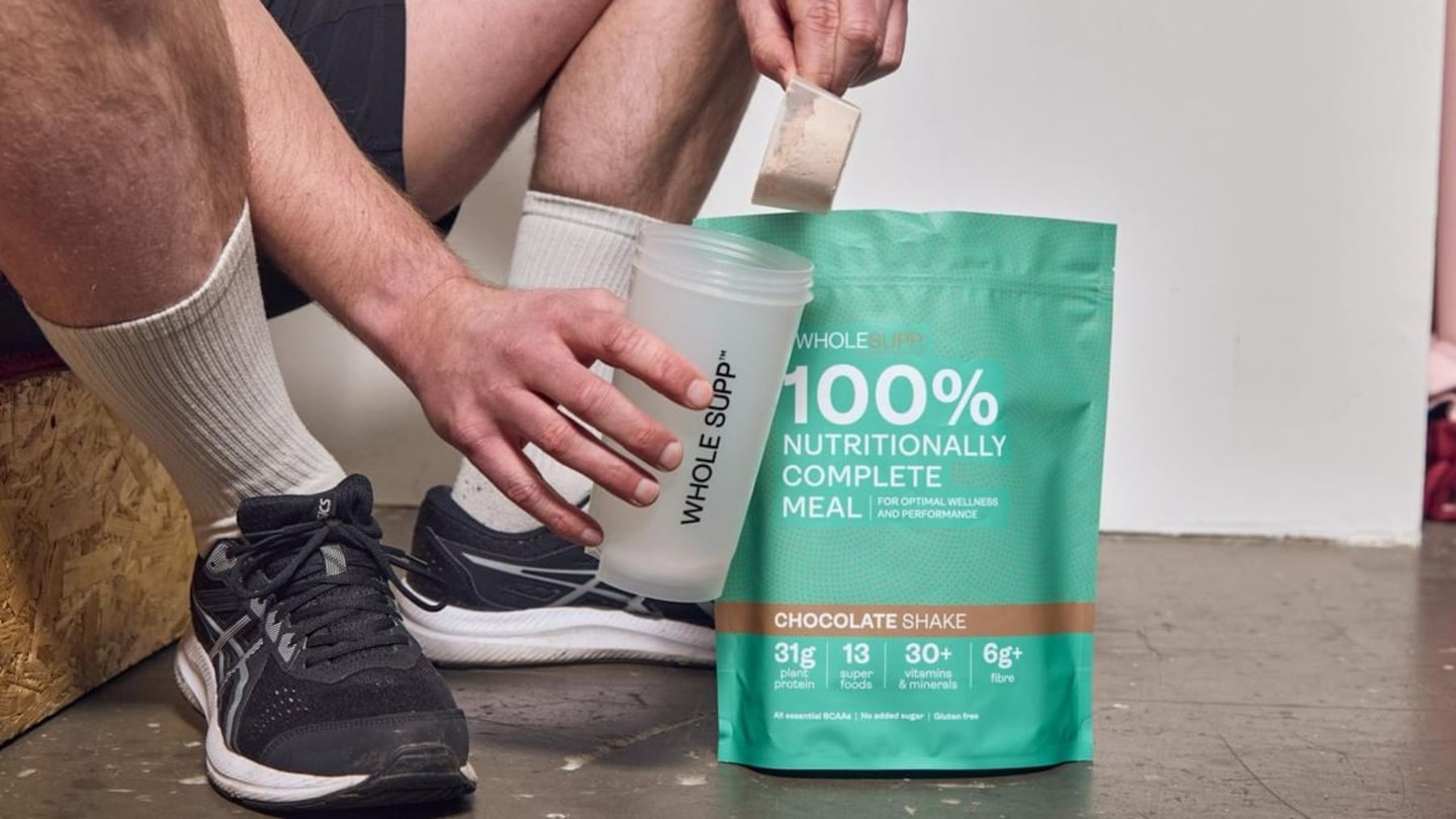 A man scooping Whole Supp superfood meal shake into a shaker.