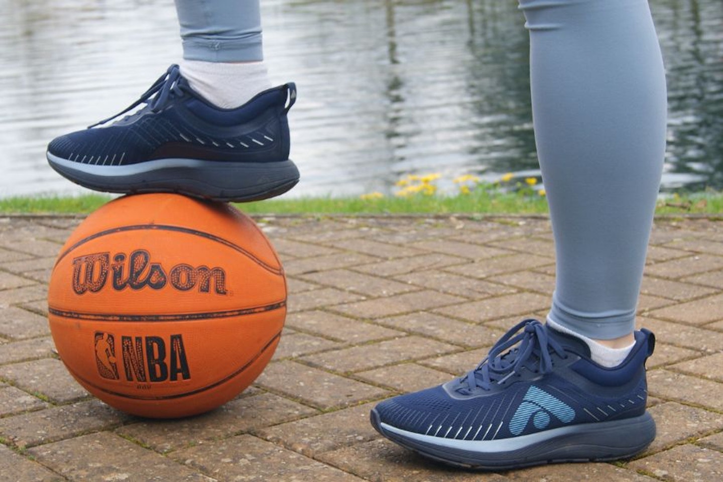 A woman wearing a pair of FitFlop FFRUNNER's with a basketball in front of a lake.