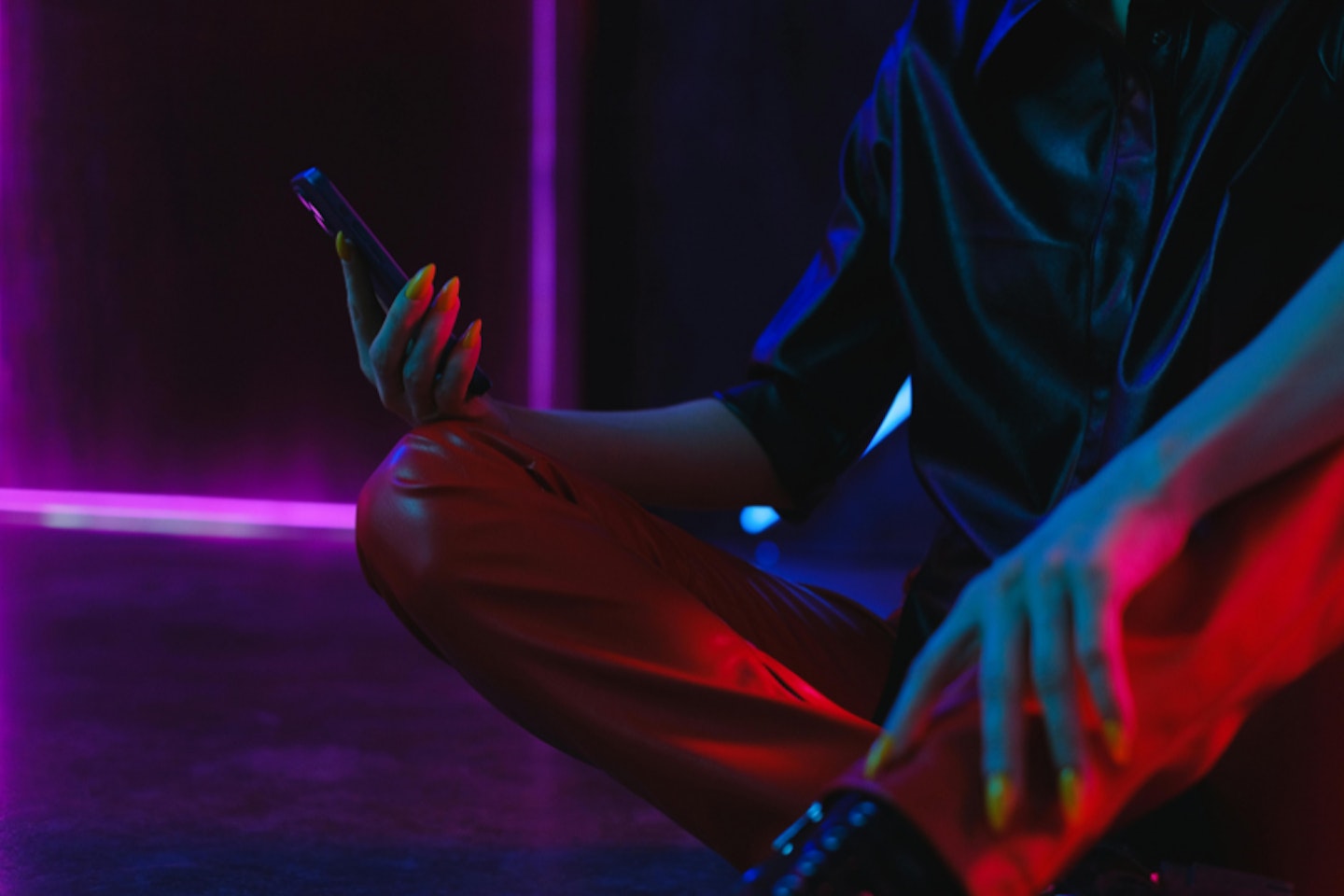 Person sitting down using a phone in a neon room