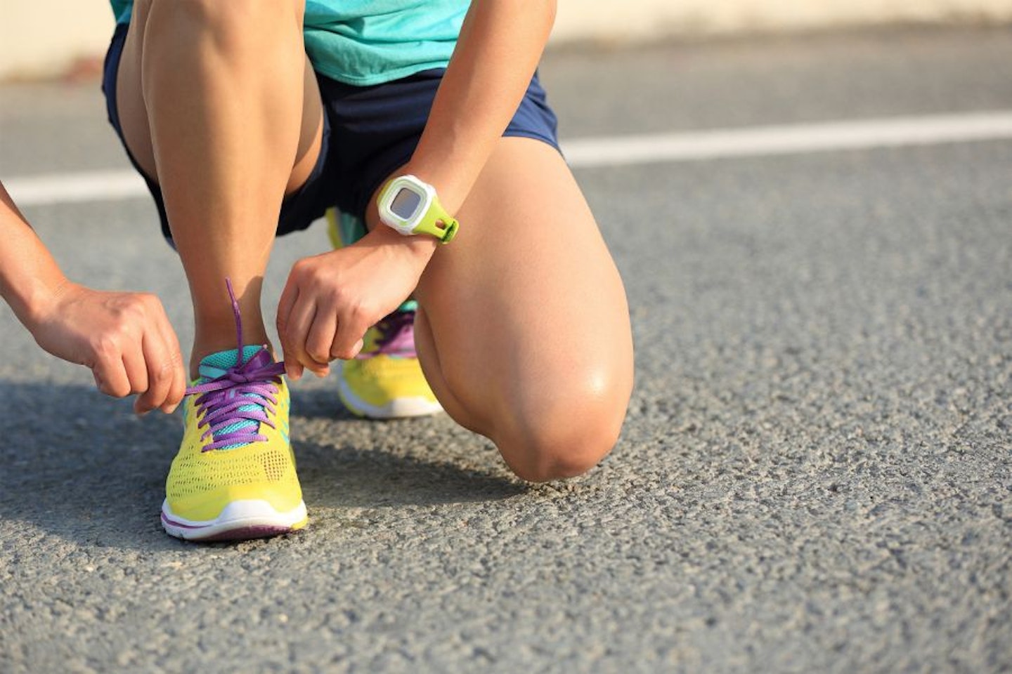 A woman lacing up her running trainers on the pavement