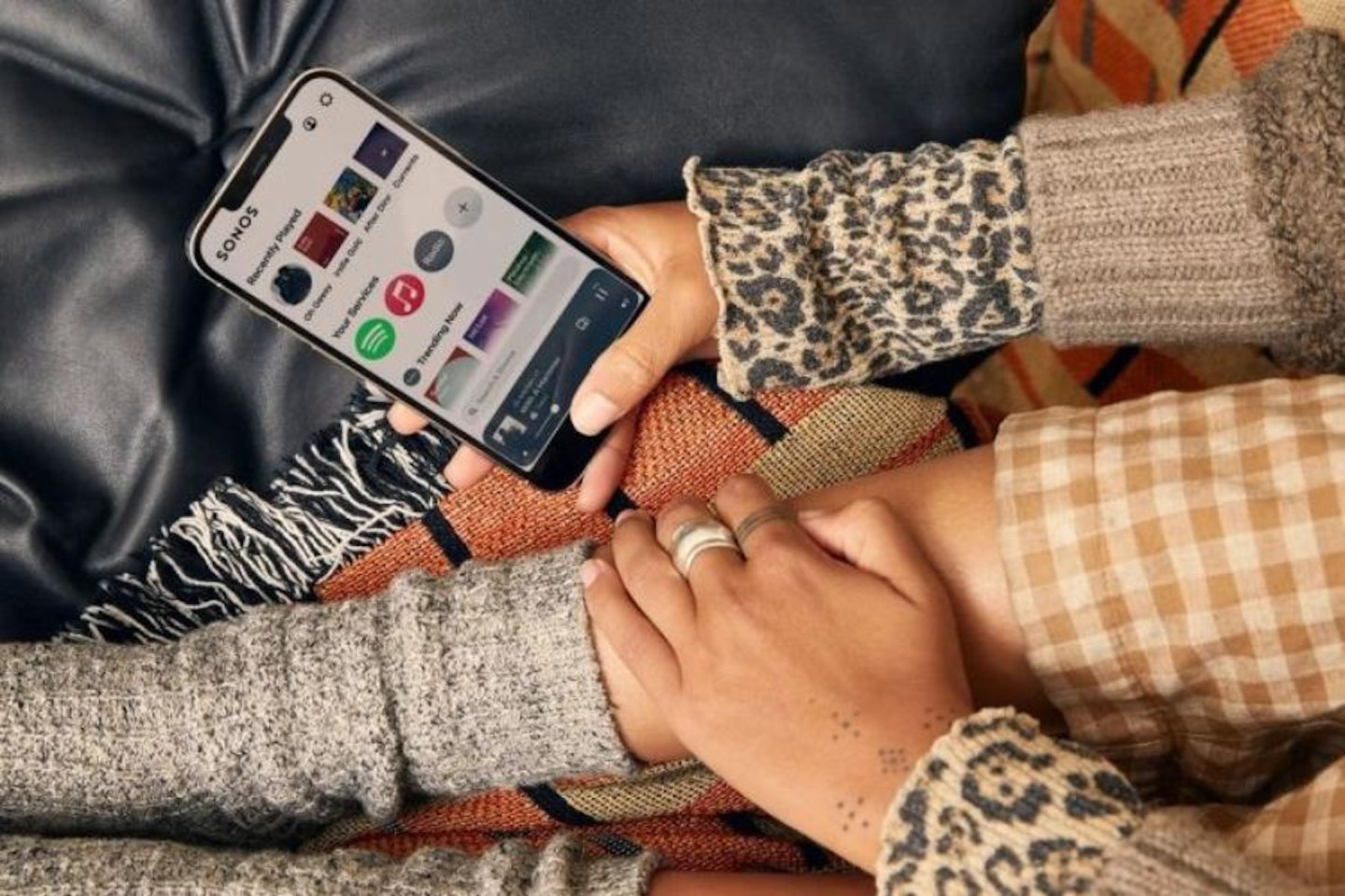 A woman sitting on a sofa using the Sonos App