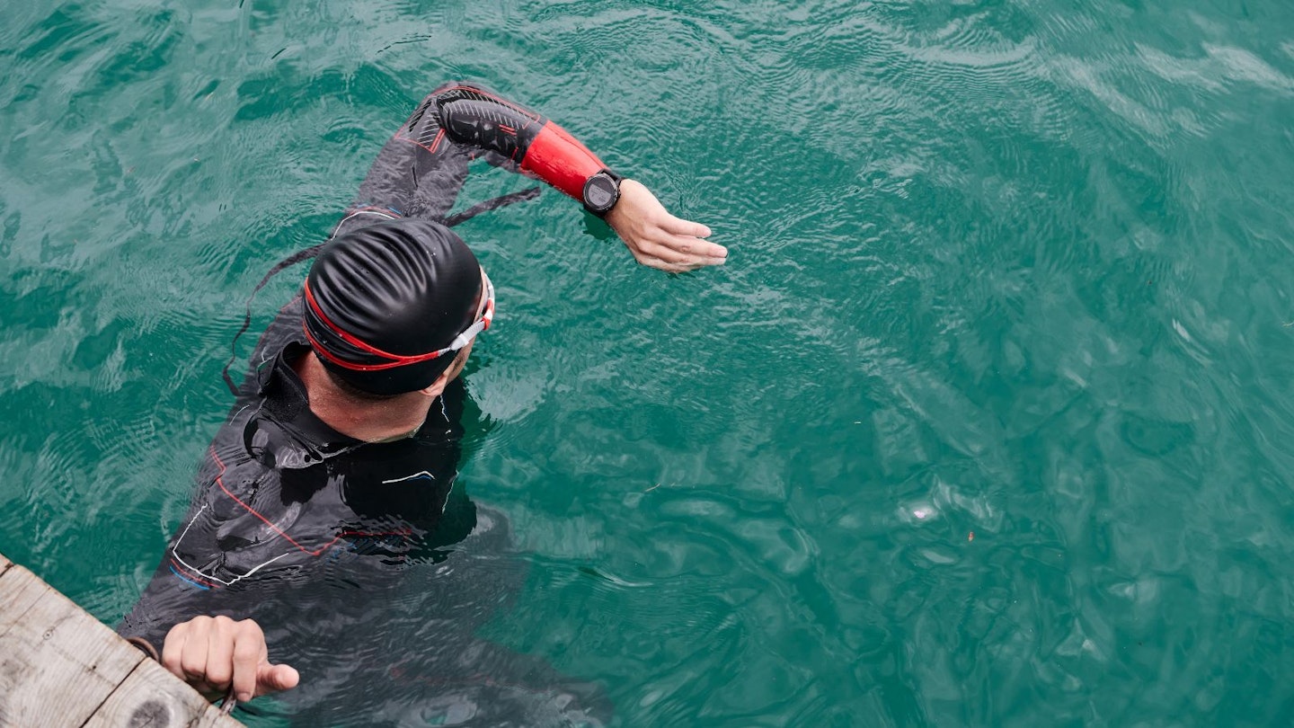 triathlon athlete swimming on morning training in lake wearing wetsuit and setting smartwatch