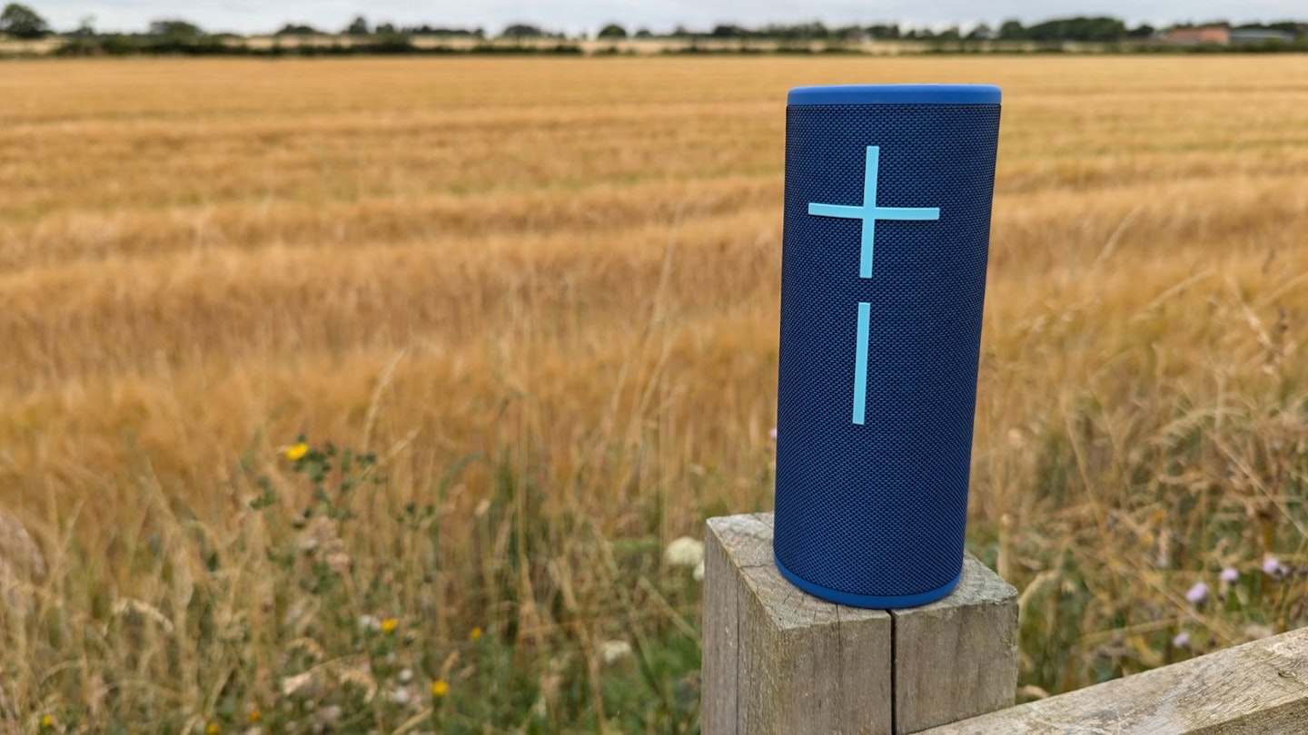 UE Boom 4 speaker on a fence post, wheat in a field behind it