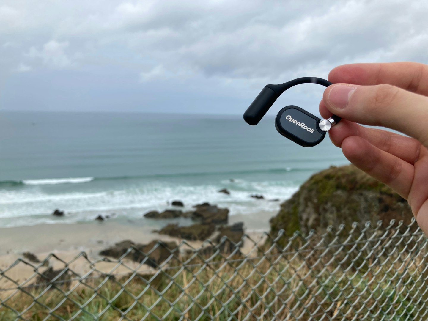 OpenRock X air conduction earbud shown with ocean and beach in background