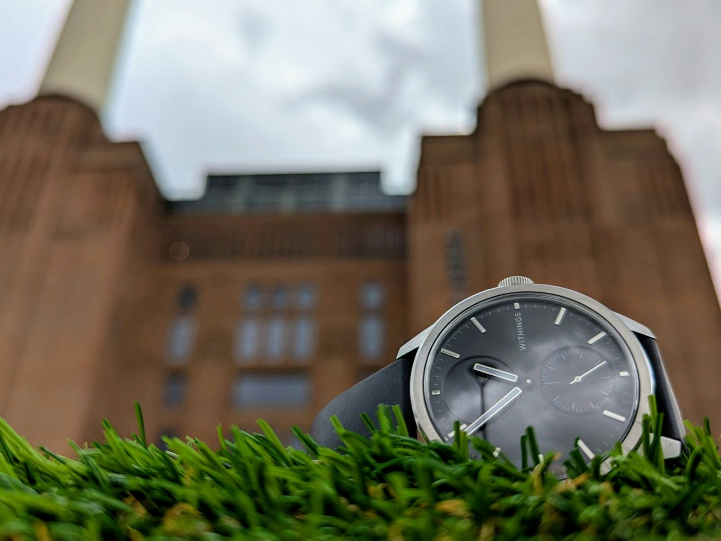 Withings ScanWatch 2 lying on grassy surface, with Battersea Power Station in the background