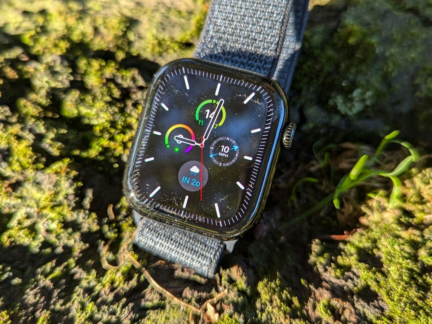 Apple Watch Series 10 displaying complications on watch face, on mossy surface