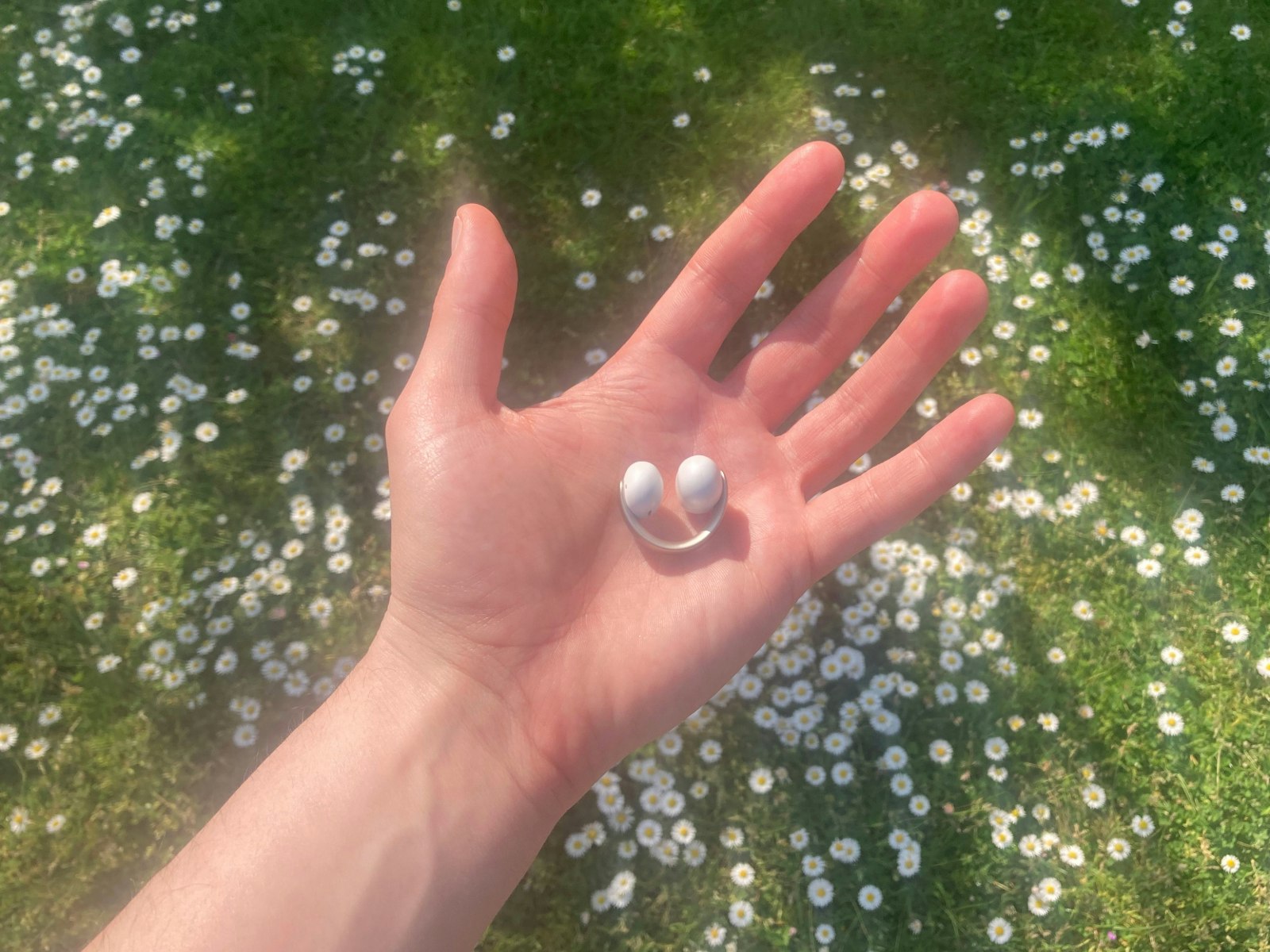 Soundcore AeroClip earbud being held in hand in front of grass and daisies