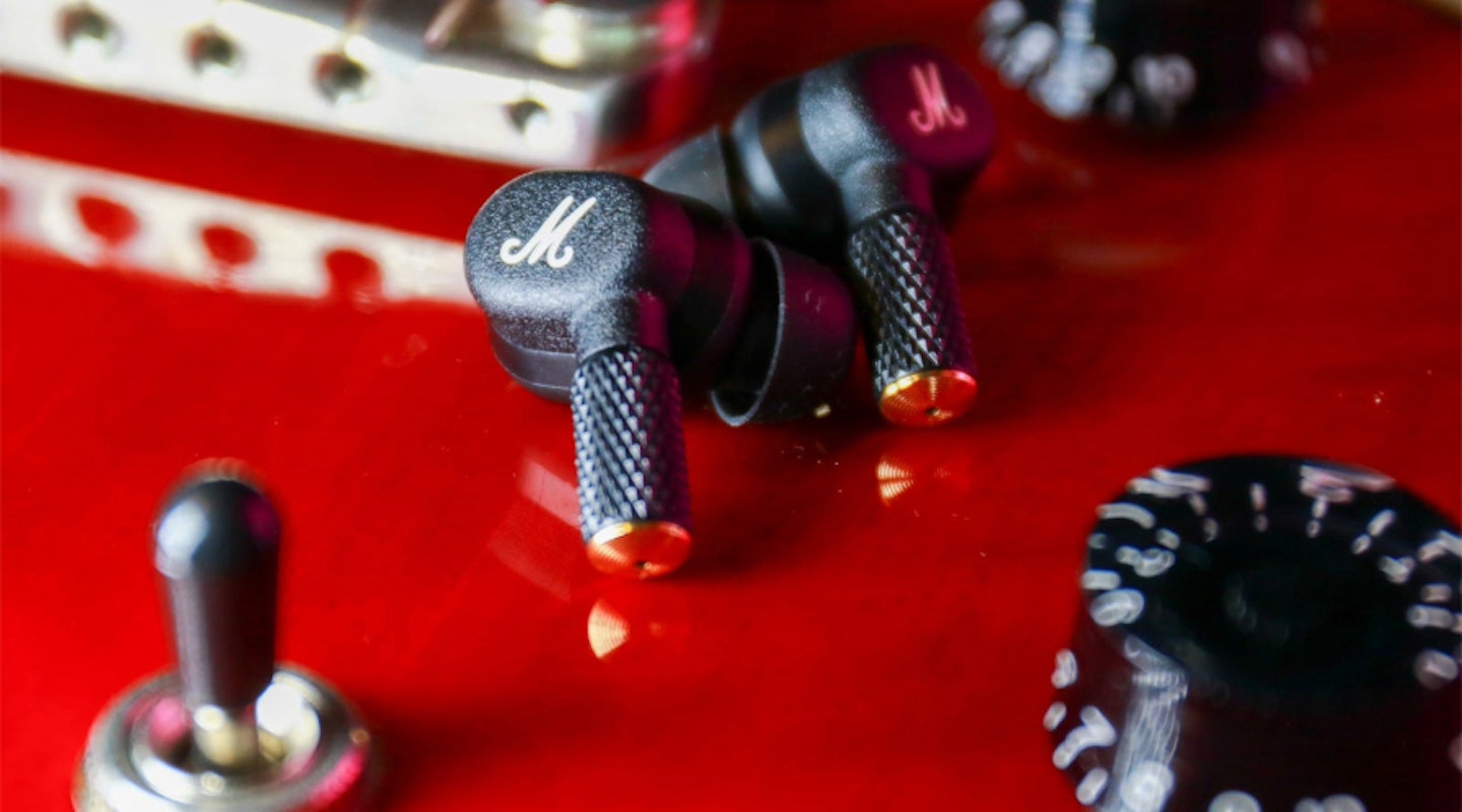 Marshall Motif II ANC earbuds. Noise-cancelling headphones. Alternatives to Sony WF-1000XM5, Jabra Elite and Bose QuietComfort Ultra. Shown on top of red electric guitar.