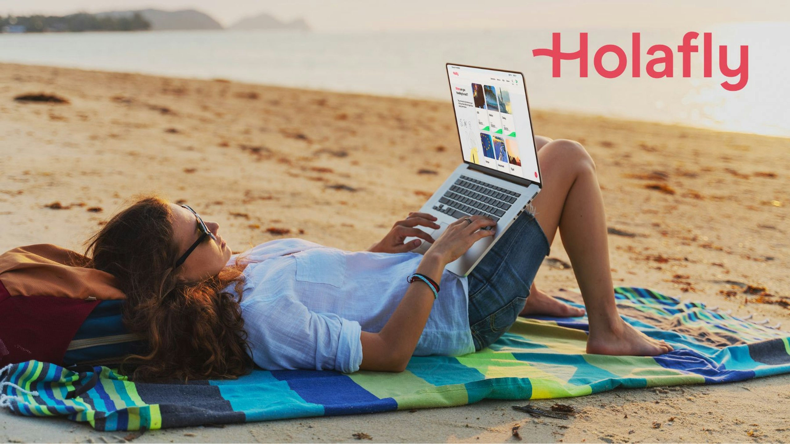Holafly eSIM - a woman on holiday ona beach using a laptop