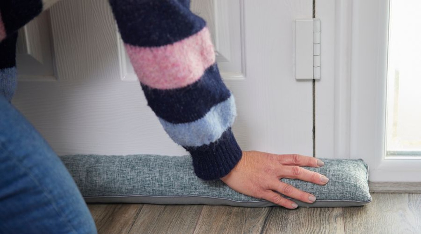 A woman fitting a door draught stopper in front of her door