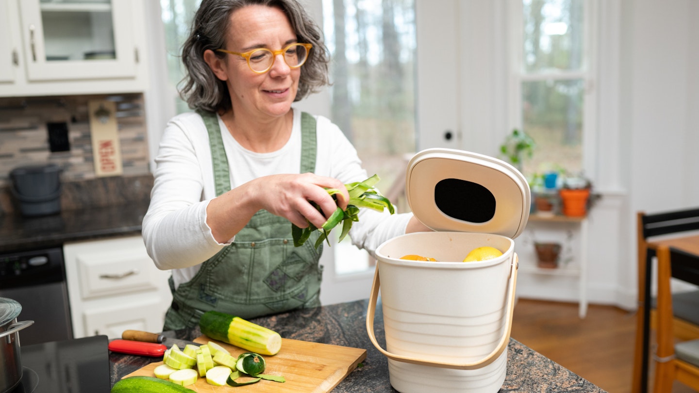 Mature women preparing a meal uses a compost bin to discard the veggie scraps