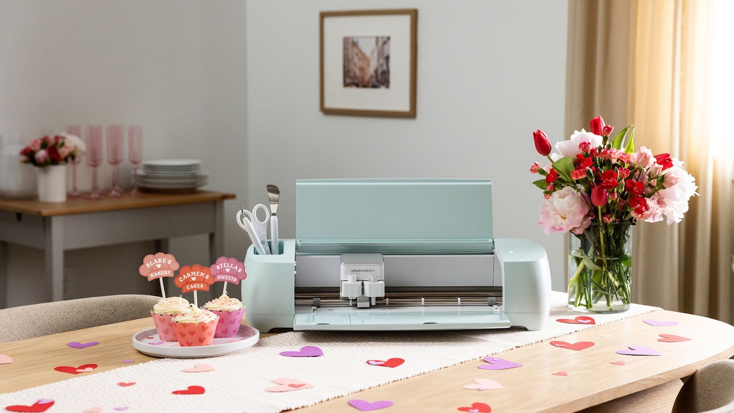 Cricut Explore machine on a home table top with Valentine's Day decorations, cupcakes and flowers