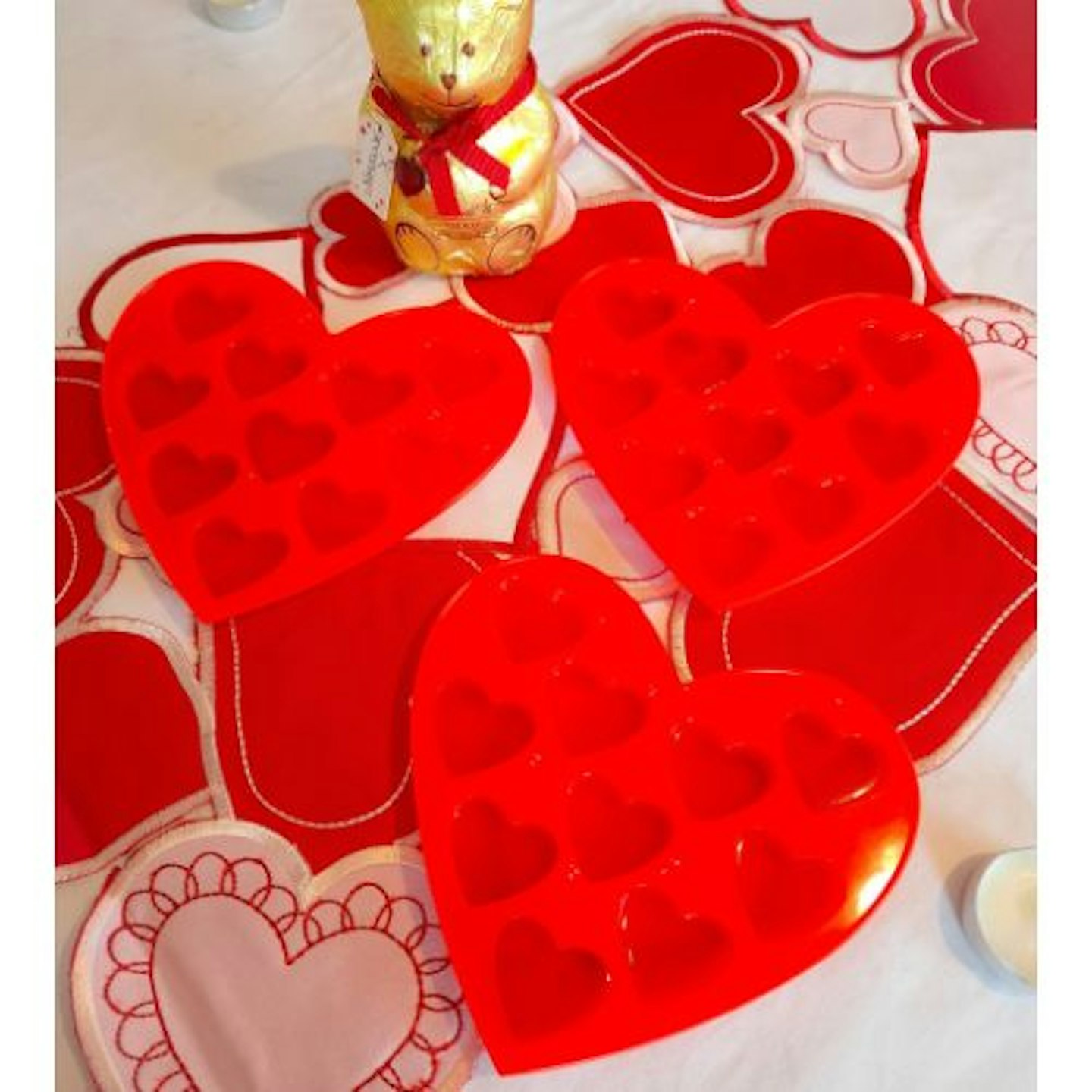 three Silicone Chocolate Moulds on a heart-patterned table cloth with a gold chocolate bear in the background