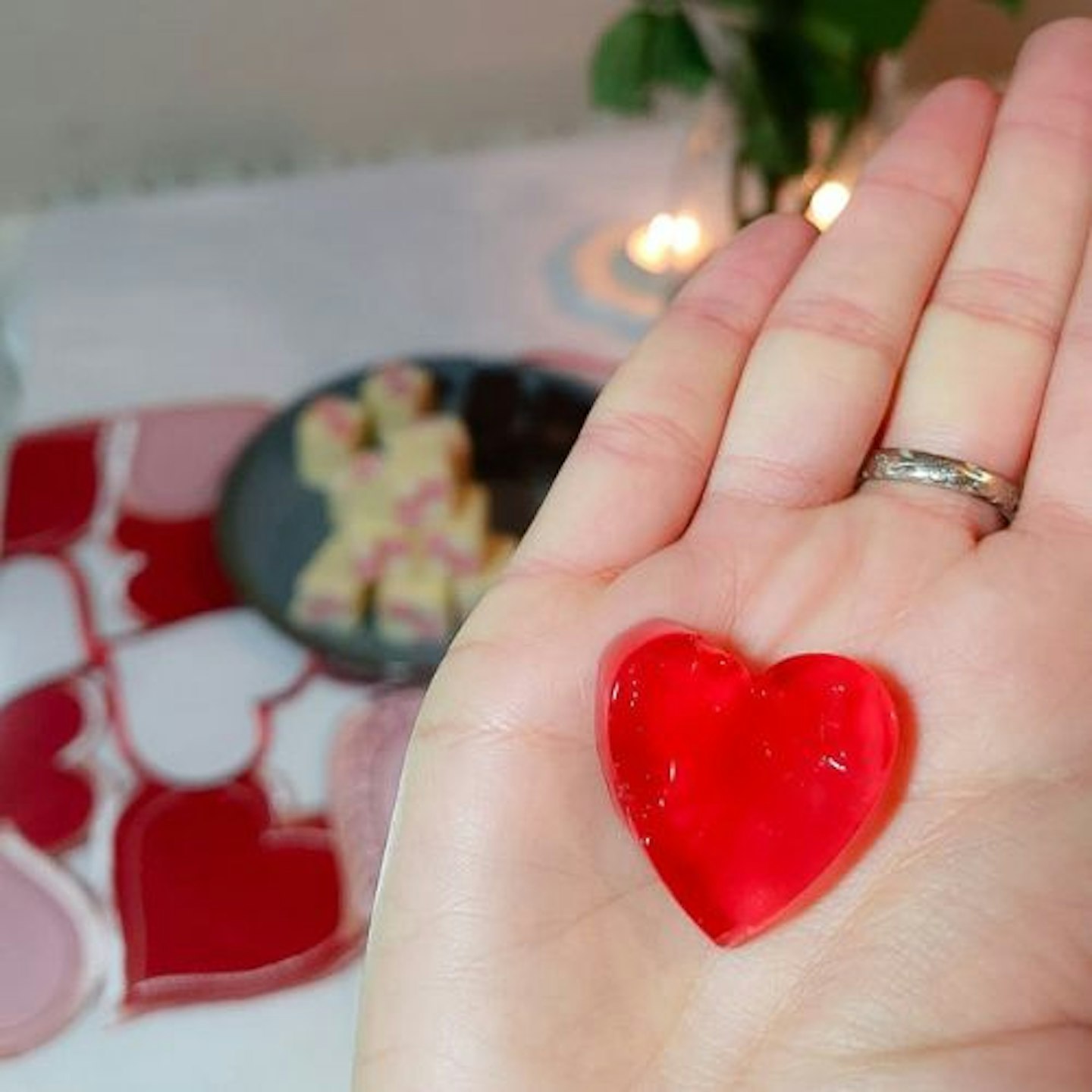 a perfect heart-shaped red jelly in the tester's palm with cakes on a table in the background