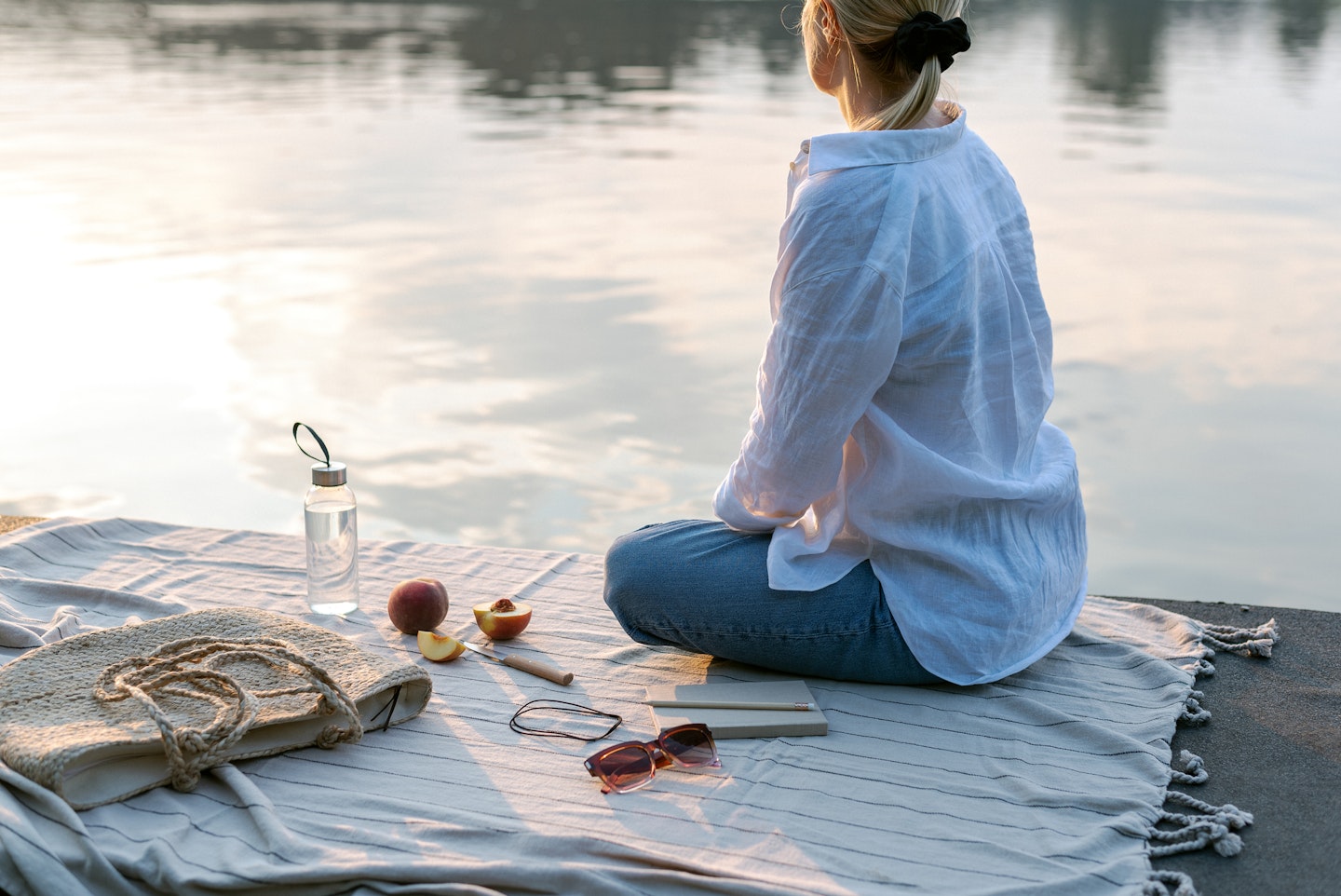 Summer Picnic By The Lake At Sunset. Woman Relaxes In Nature.