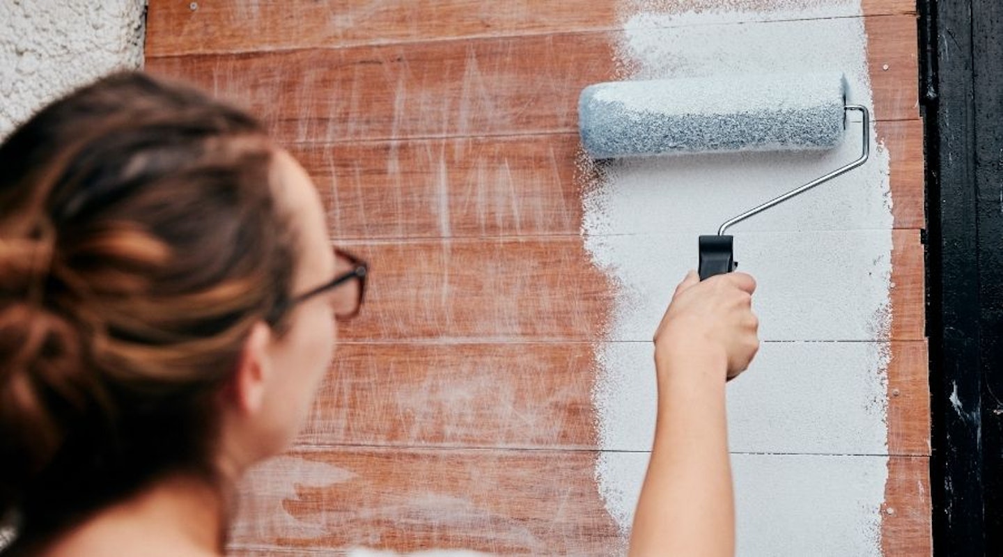 A woman using a roller brush to paint her shed