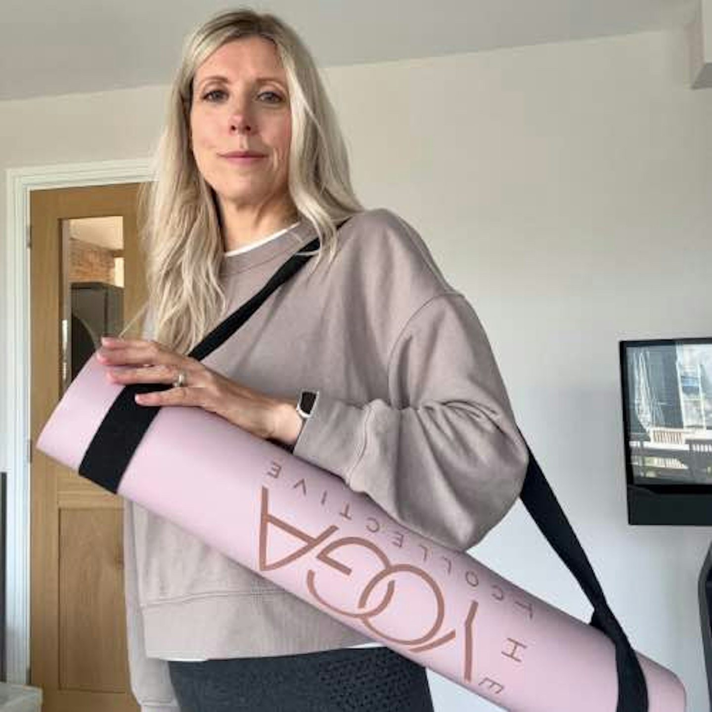 Female with long blonde hair holding a pink yoga mat 