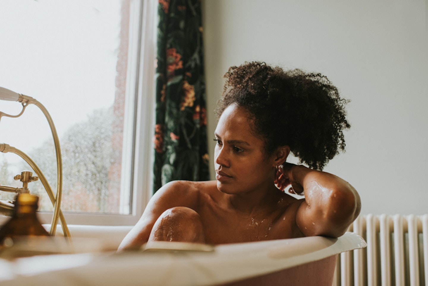 A beautiful woman daydreams in a roll top bathtub. She seems distracted as she looks at nothing in-particular.