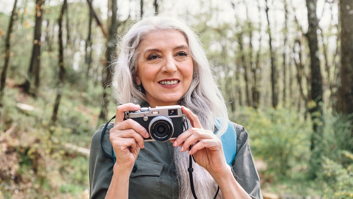 Mature woman with long grey hair photographing in forest, Scandicci, Tuscany, Italy - stock photo