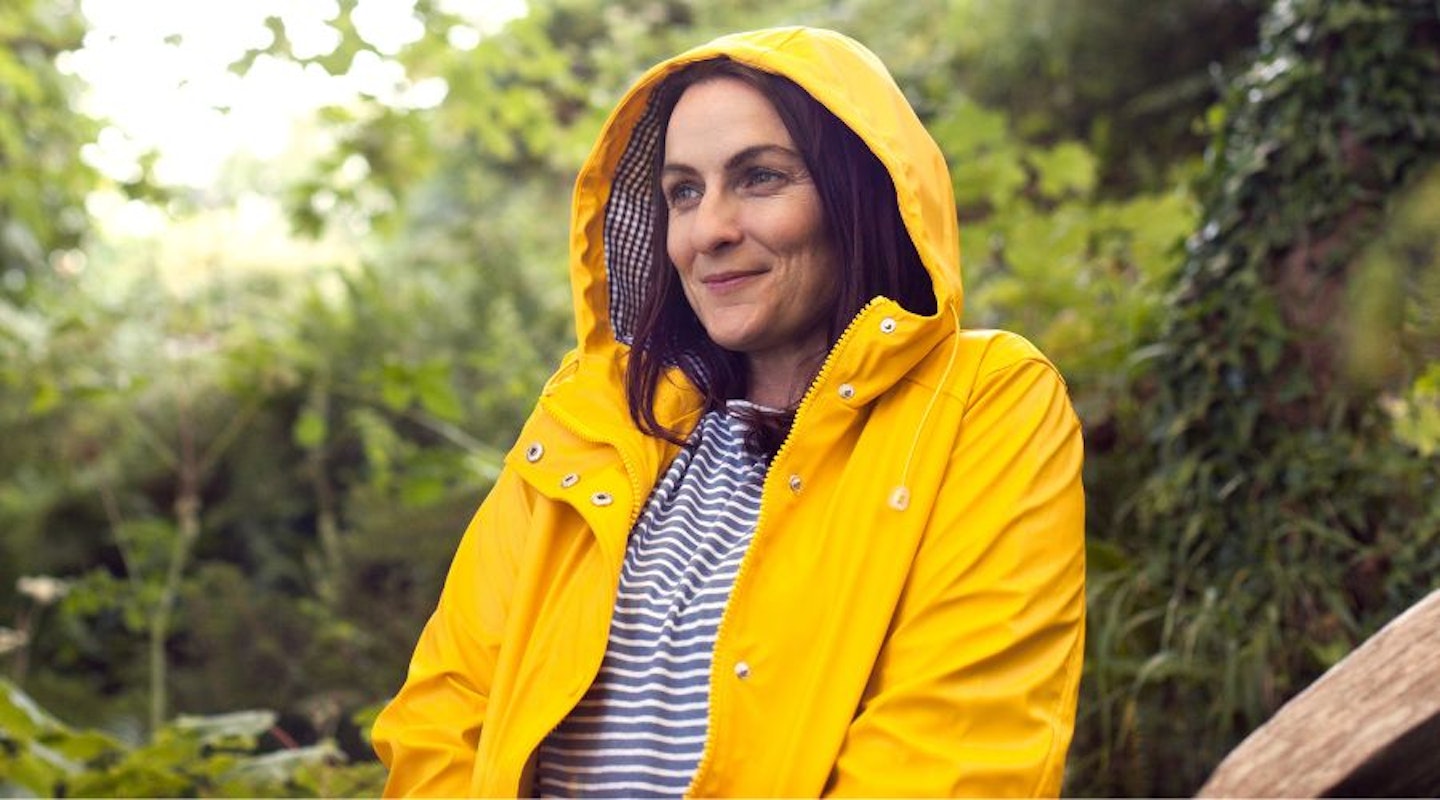 A lady wearing a stylish yellow raincoat with the hood up