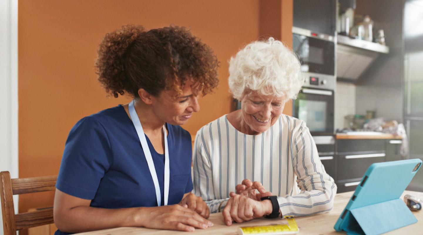 A carer showing an elderly woman a fall detection device