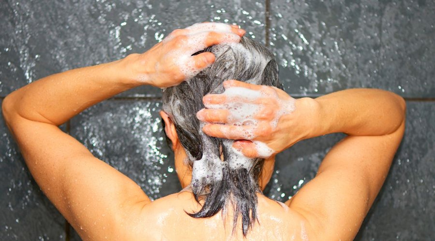 A woman washing shampoo through her grey hair in the shower