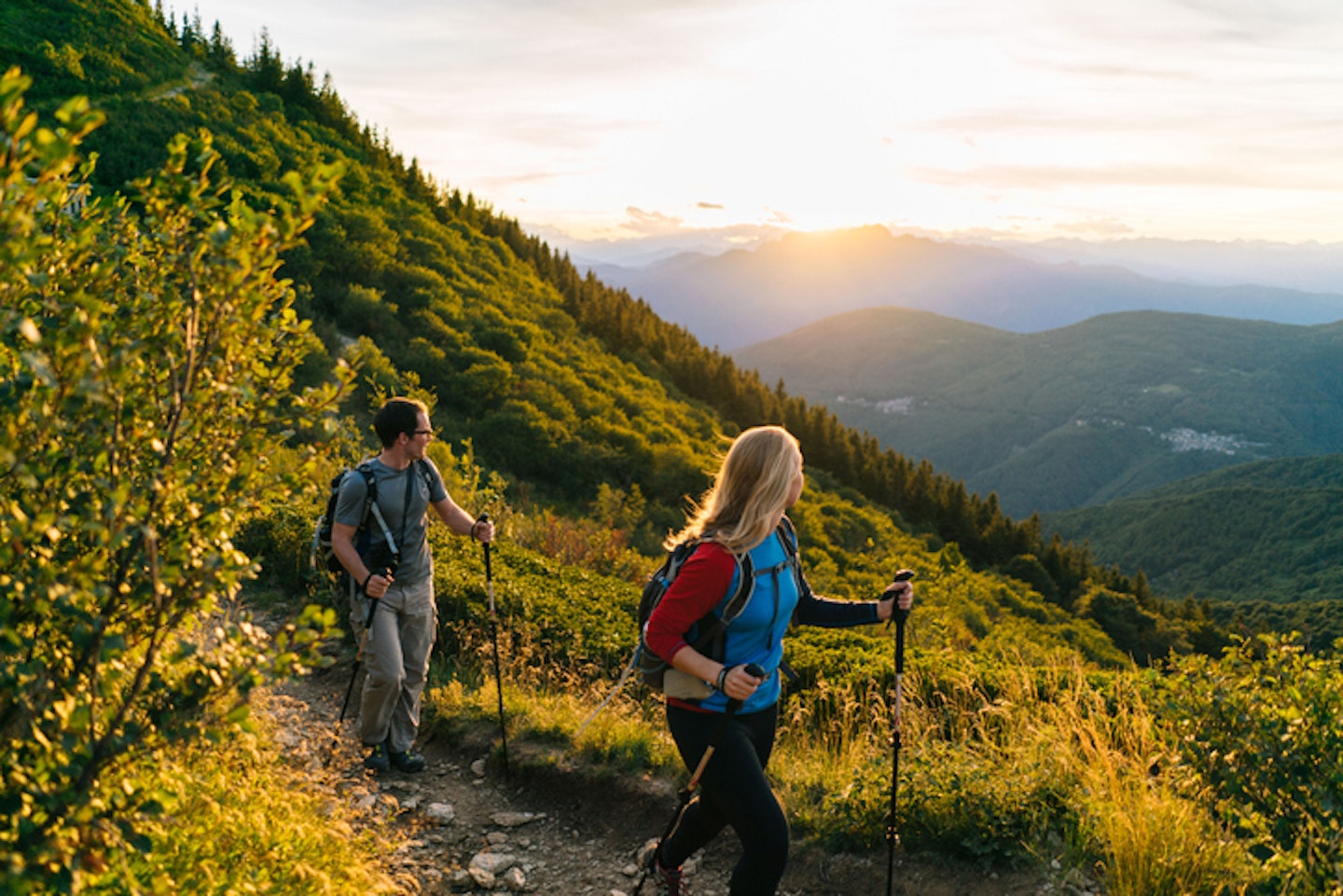 Couple hike along trail at sunrise, mountains