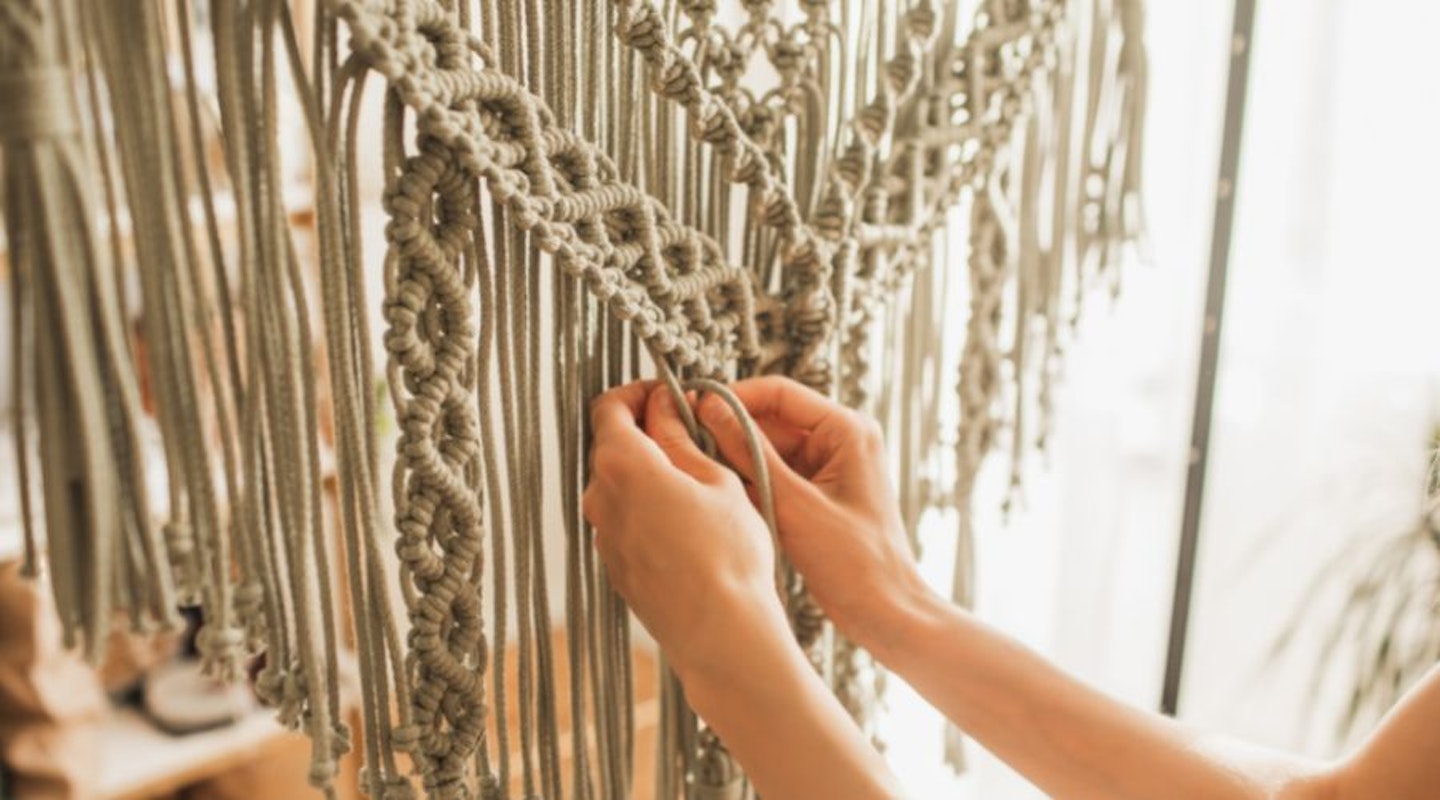 A woman using a macramé kit to create a wall hanging