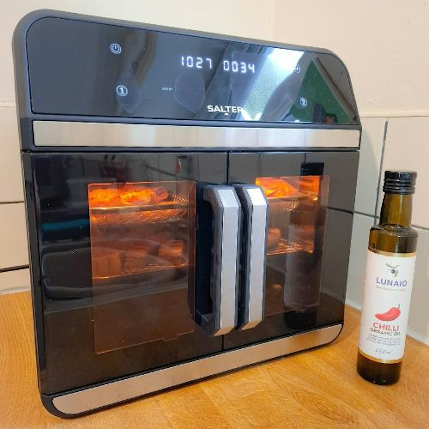 Front view of the Salter French-Door Style XL Air Fryer Oven with food cooking and a bottle of organic chilli oil