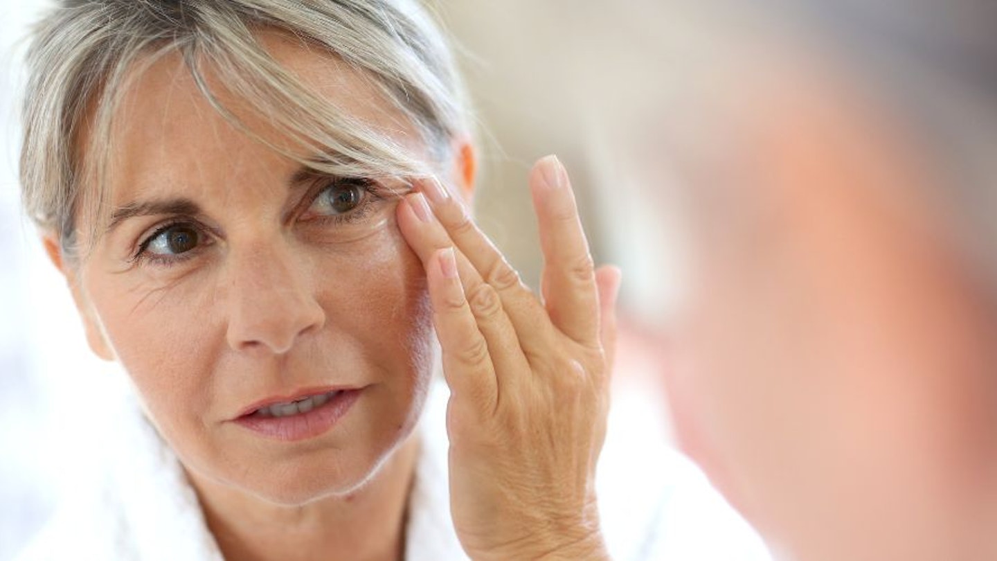 Middle-aged woman applying cream on face - stock photo
