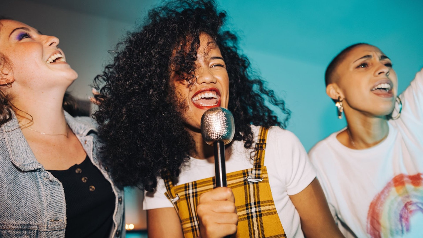 Karaoke time. Vibrant young woman singing into a microphone while partying with her friends at night. Group of happy female friends having a good time together on the weekend.