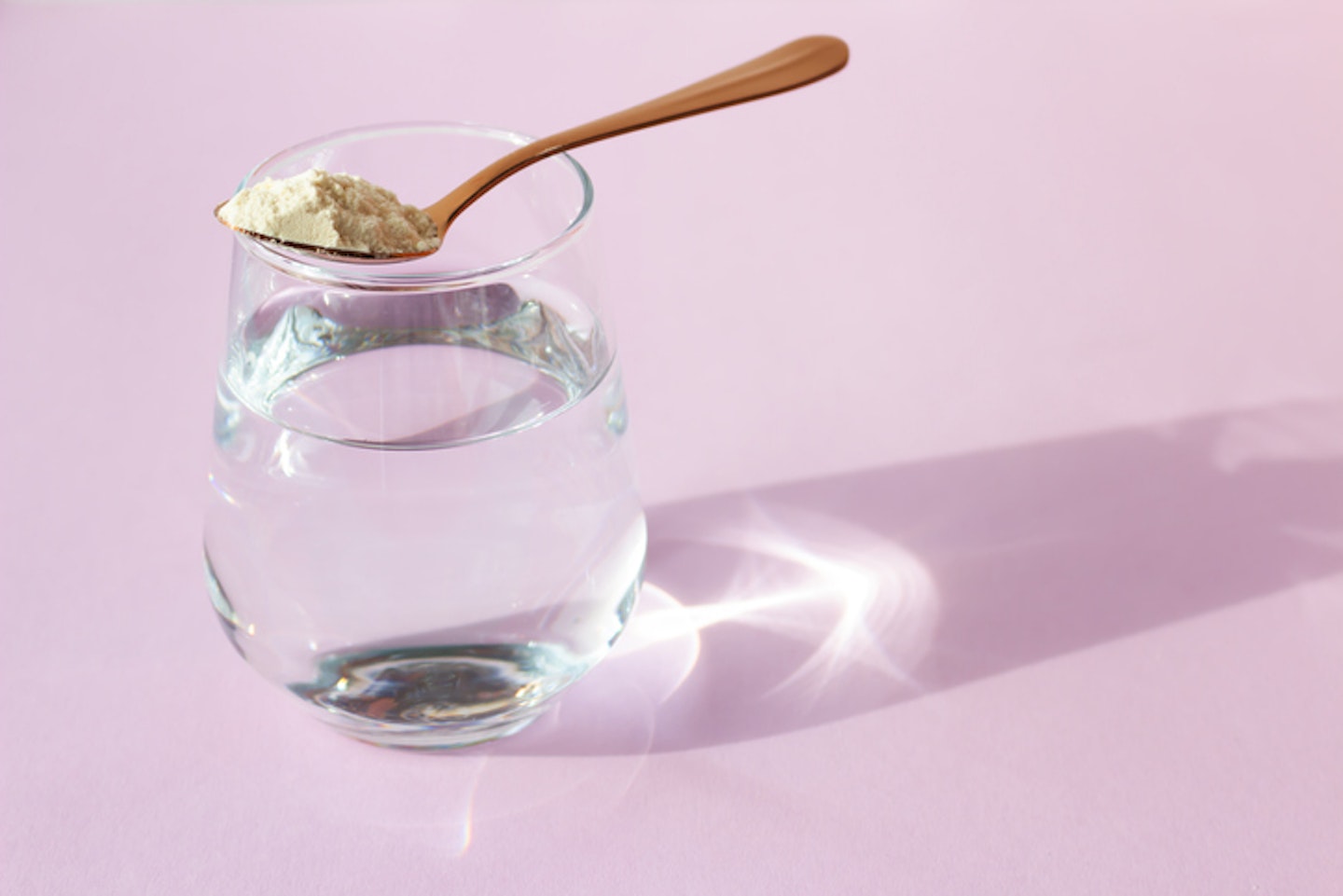 Collagen powder in a spoon and a glass of water on a pink background. Beauty concept. Place for your text