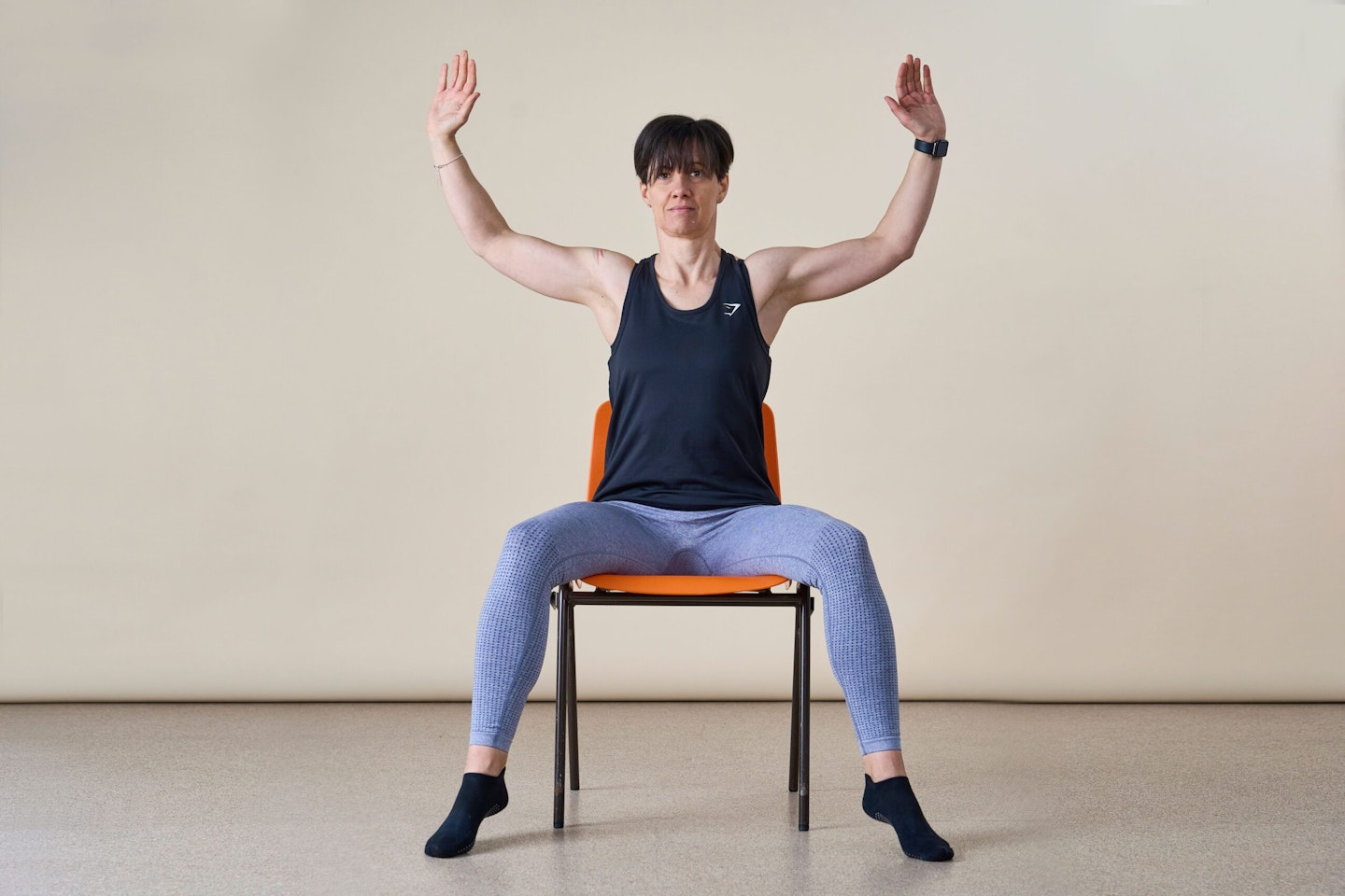 Woman facing camera doing a seated jumping jack while sitting in a chair