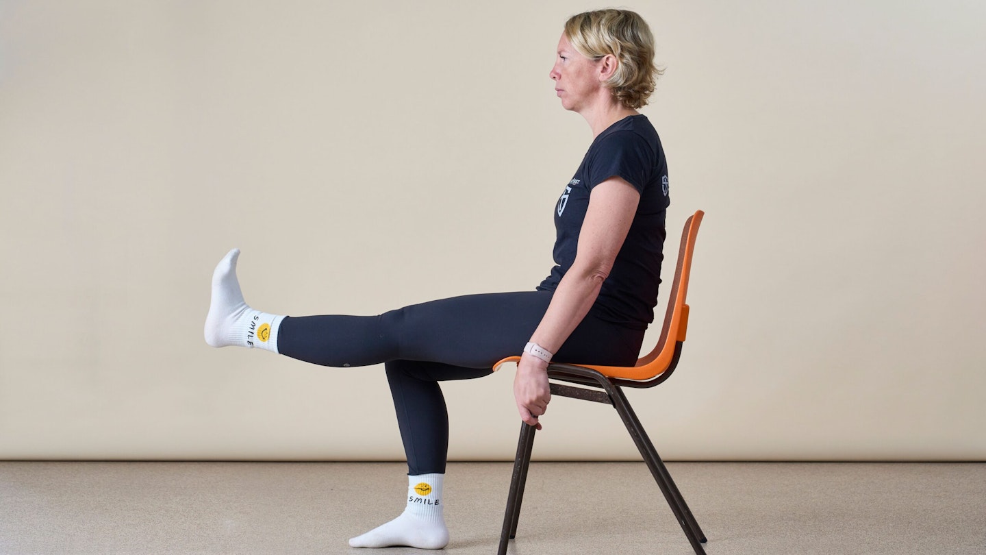 Woman sideways to camera doing a seated leg extension sitting on a chair