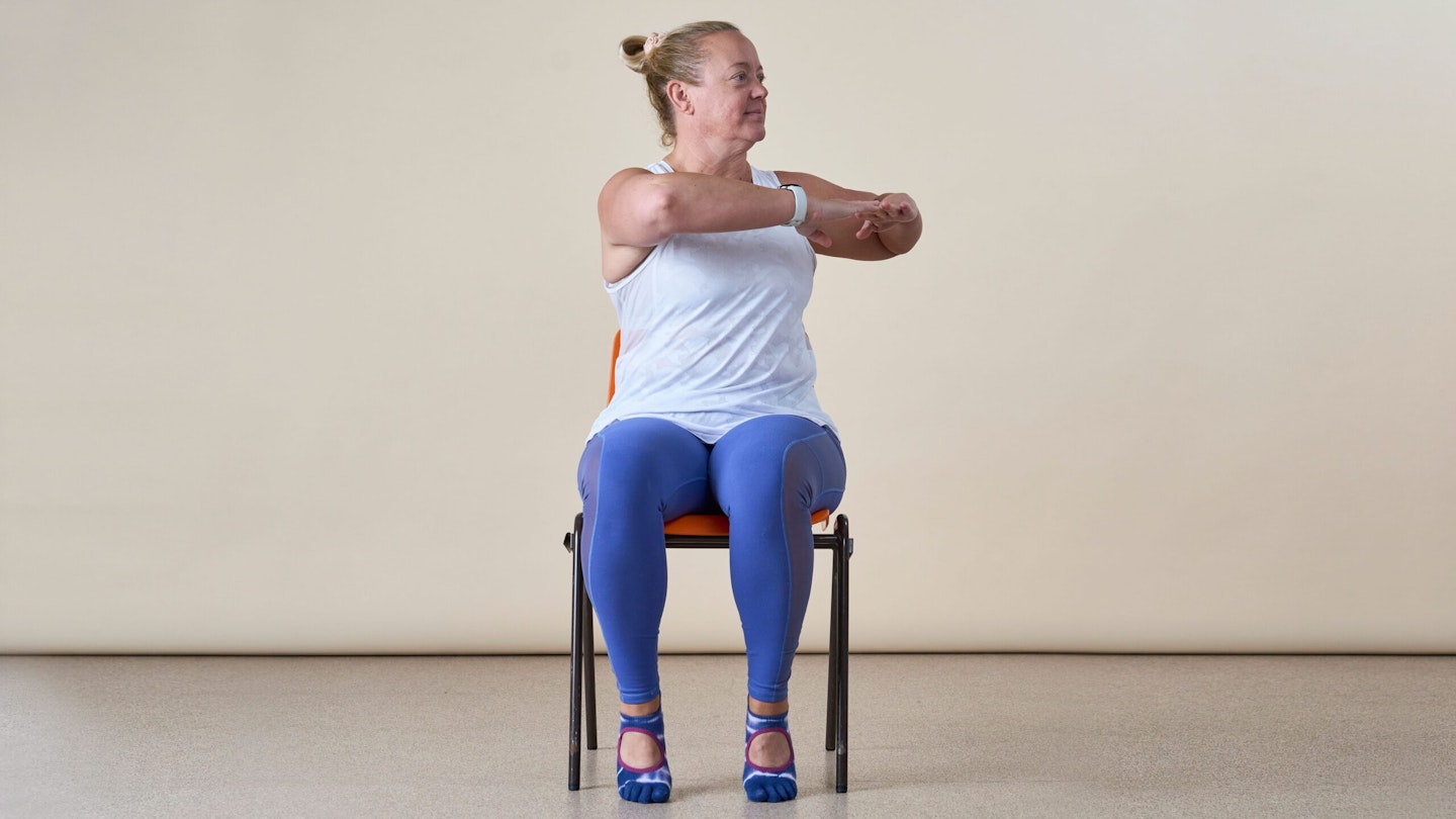 Woman in a chair twisting her torso away from the camera. Her arms are extended with elbows bent