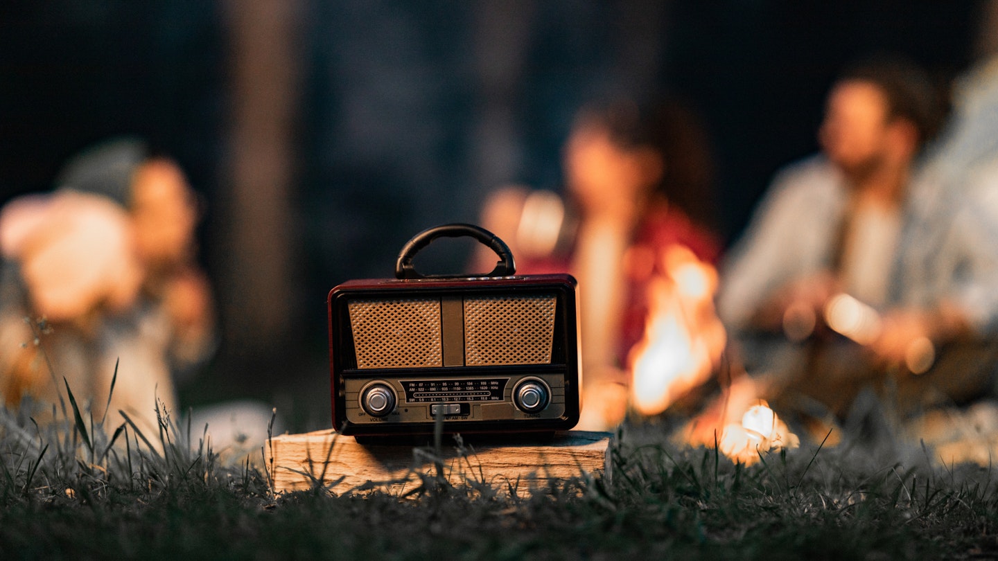 Close-up of a vintage radio during camping night with people in the background.