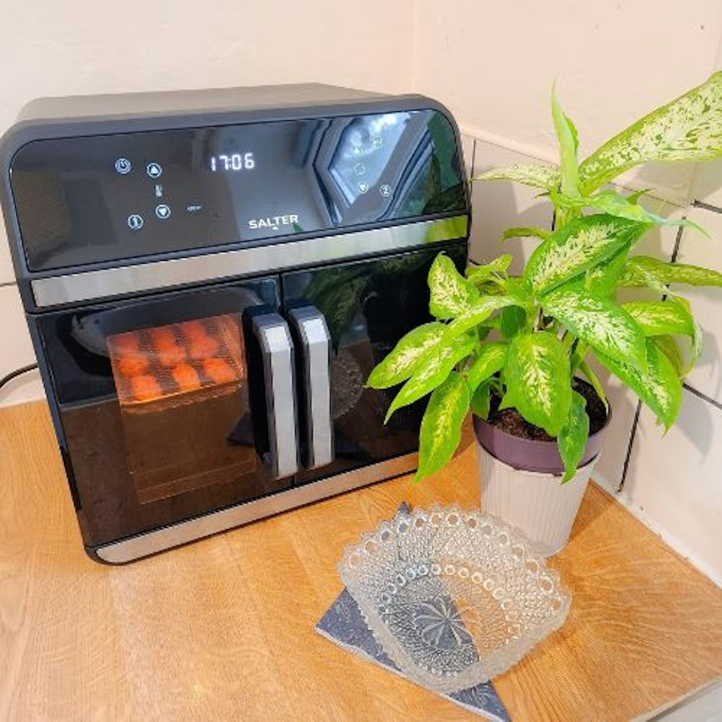 photo of Salter French-Door Style XL Air Fryer Oven on countertop with snacks air frying in one compartment, a green leafy plant and serving dish are in front of the appliance