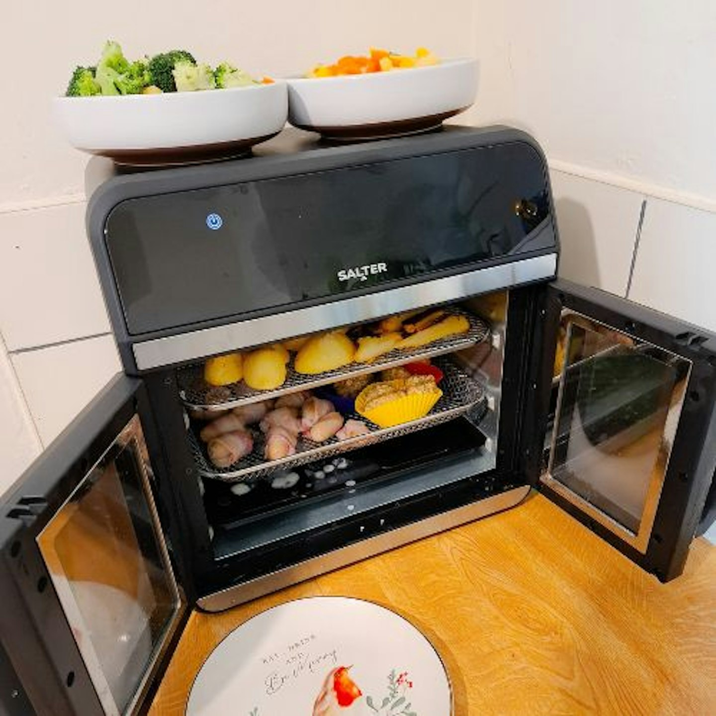 photo of Salter French-Door Style XL Air Fryer Oven, door wide open, showing whole cooking space being used to cook colourful roast dinner sides, including roast potatoes, pigs in blankets and stuffing