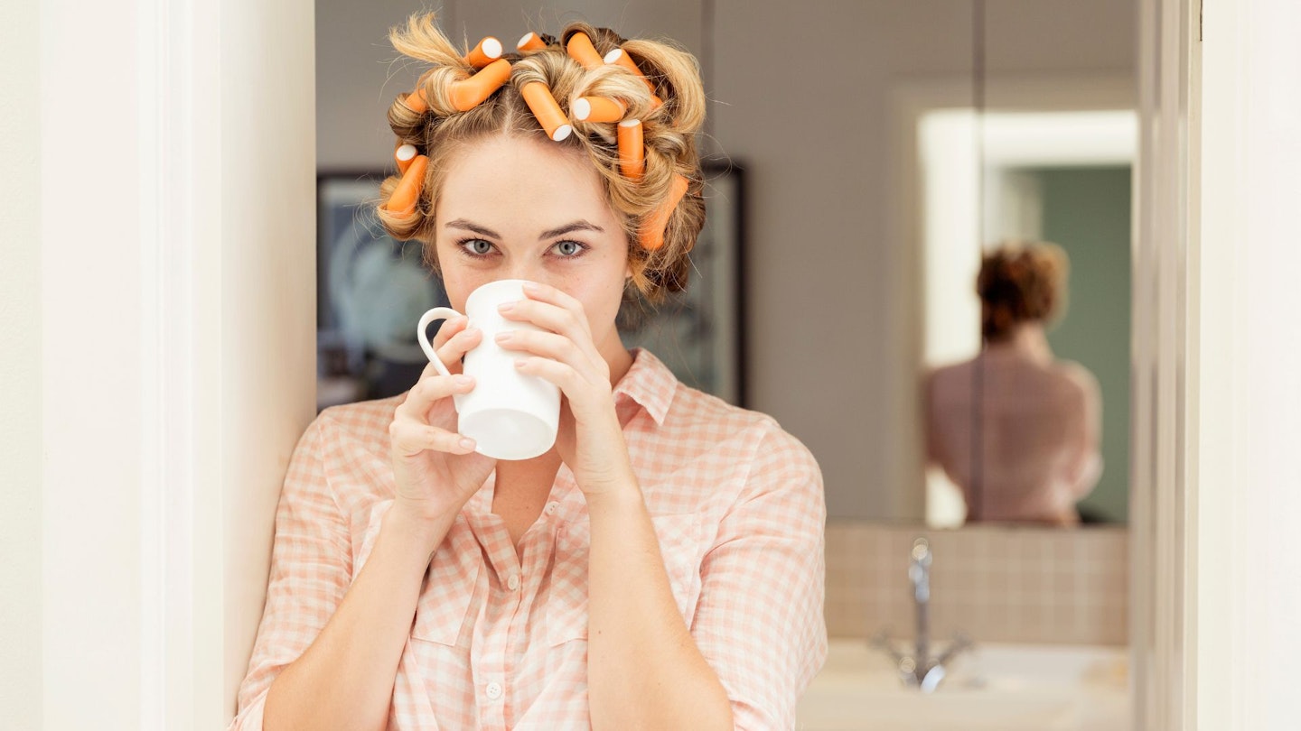 Portrait of young woman with curlers in hair drinking coffee - stock photo