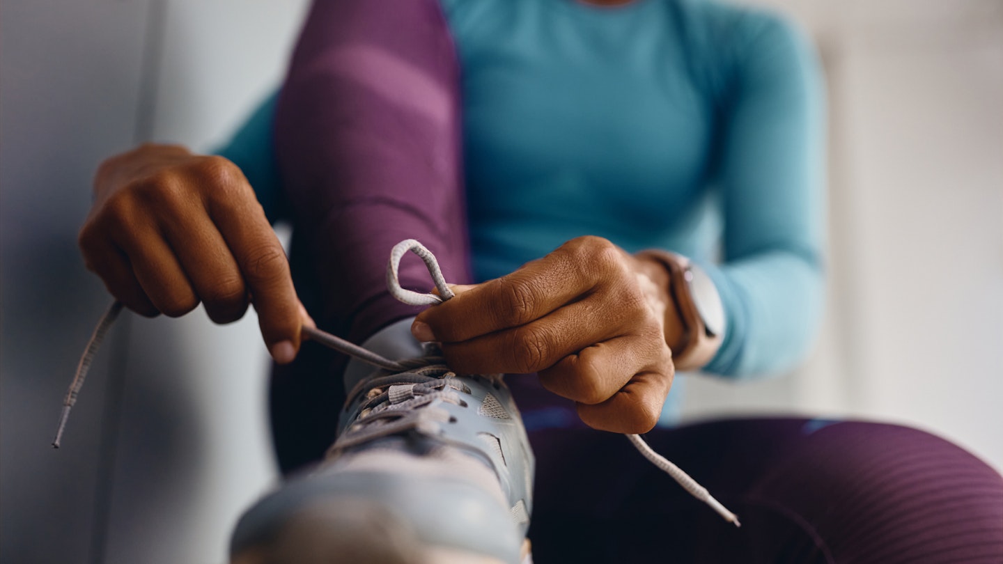 Close-up of an athletic woman tying shoelaces on sneakers while preparing for workout at health club.
