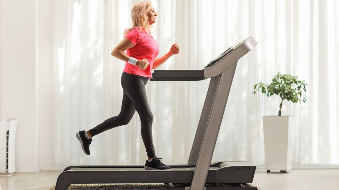 Full-length profile shot of a mature woman running on a treadmill at home
