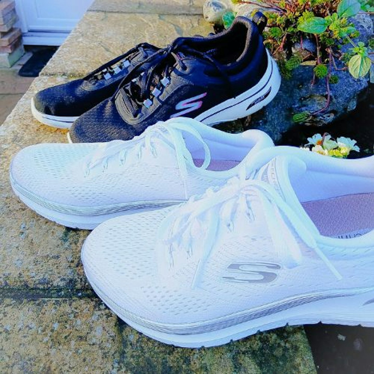 Side view of two pairs of Skechers Arch Fit trainers posed in a garden