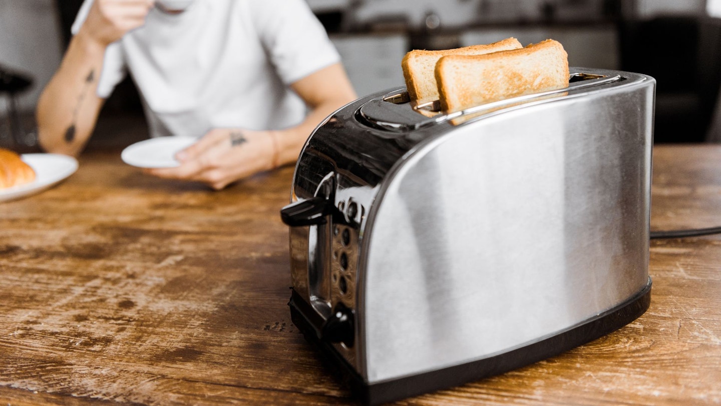 An energy efficient toaster on a table with a person behind, eating from a plate