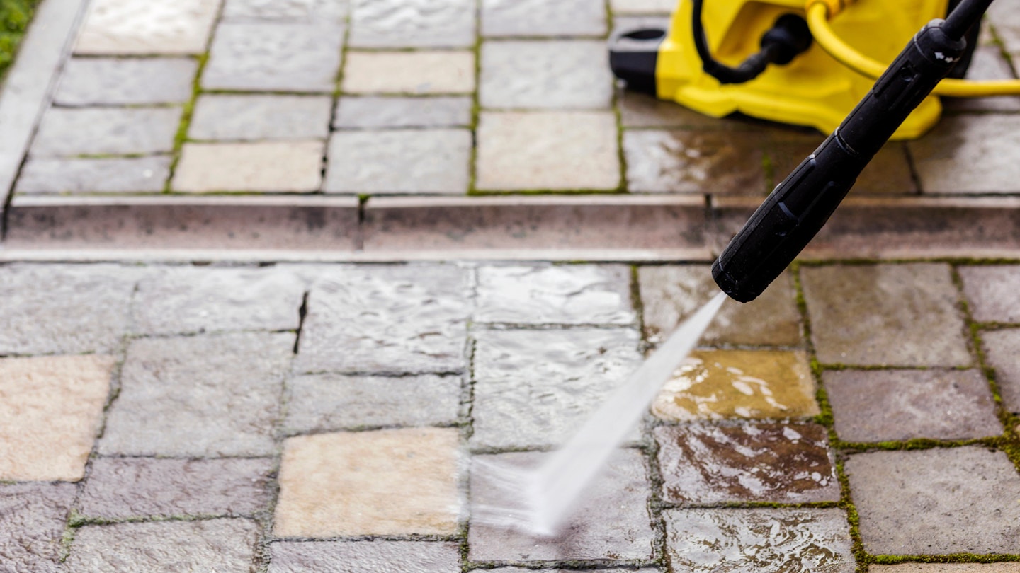 Cleaning Paving Stones in Garden with Pressure Washer. Using High Pressure Cleaner for Washing Block Pavement of Street or Home.