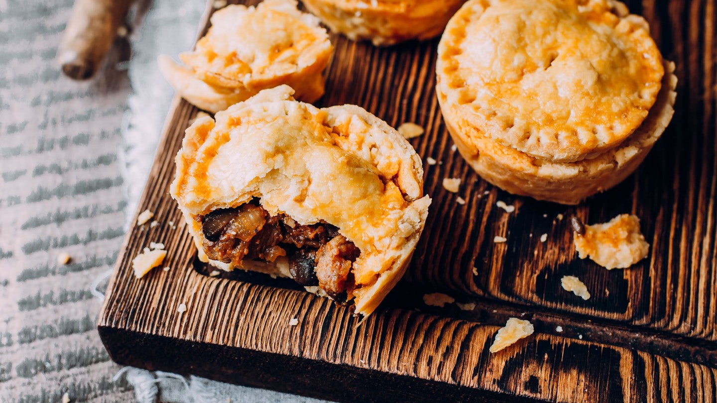 Fresh Traditional Australian meat mini pie on the wooden board on the table background, closeup with copy space, top view, rustic style.