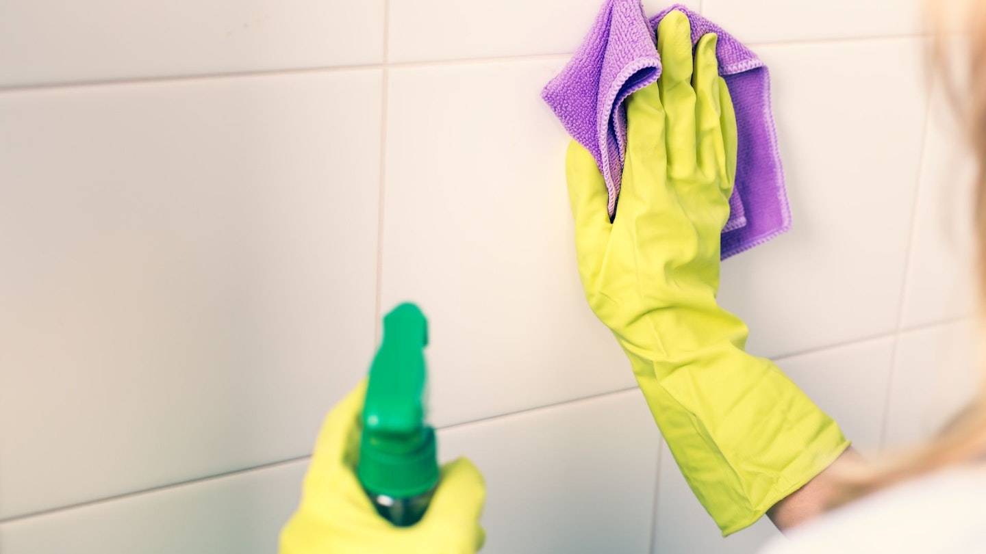 How to clean your bathroom tiles: A woman cleaning her bathroom tiles with spray and cloth