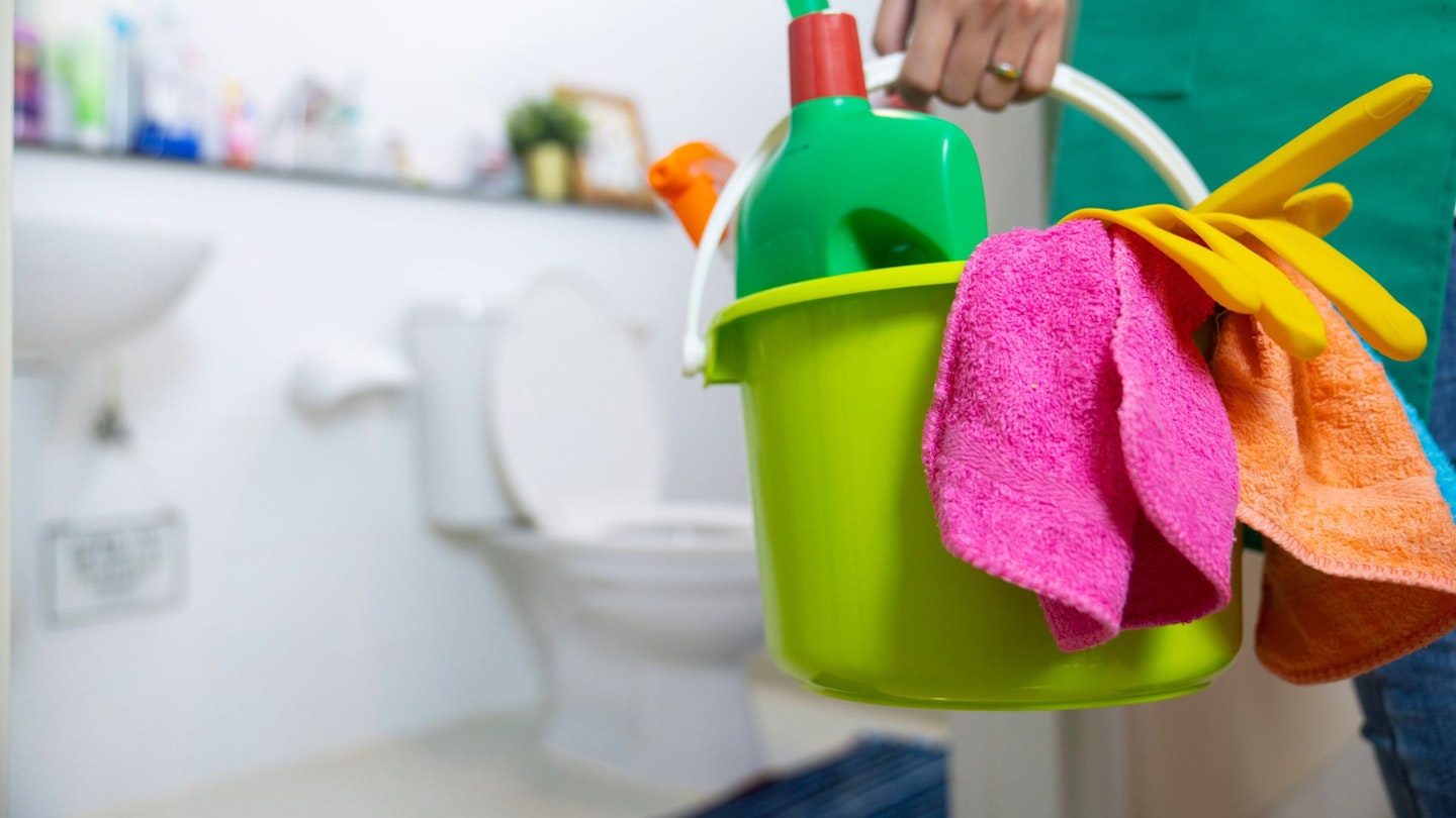 A person holding a cleaning caddy when cleaning the bathroom