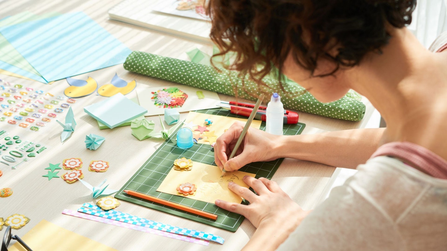 Curly haired woman making colourful greeting card decorative items and tools on table surface