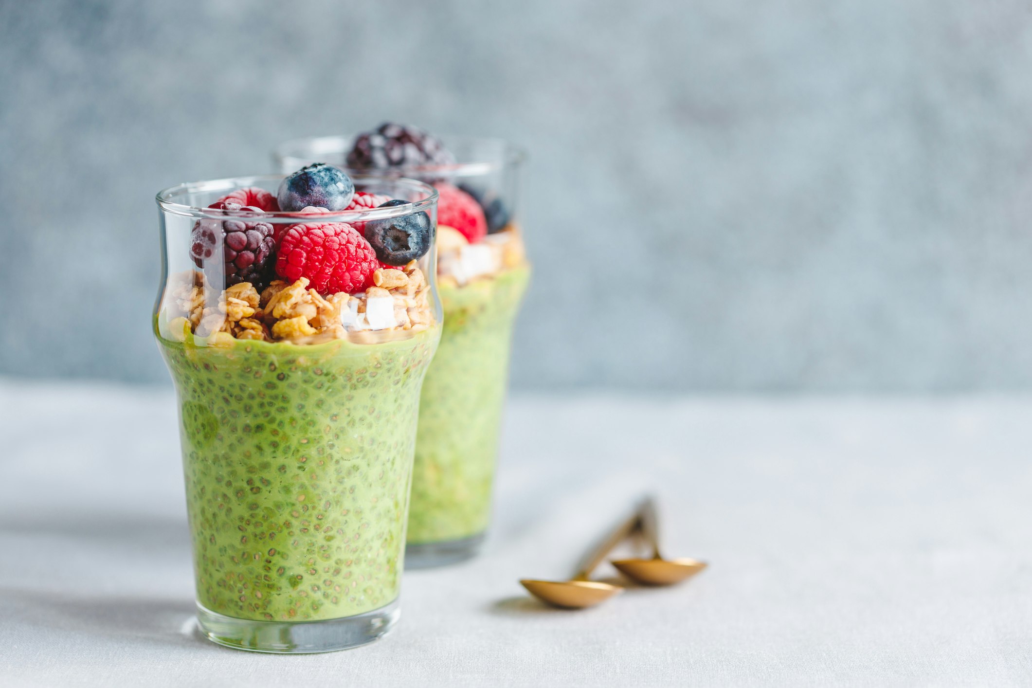 Chia pudding with matcha tea, organic granola, frozen berries in glasses.