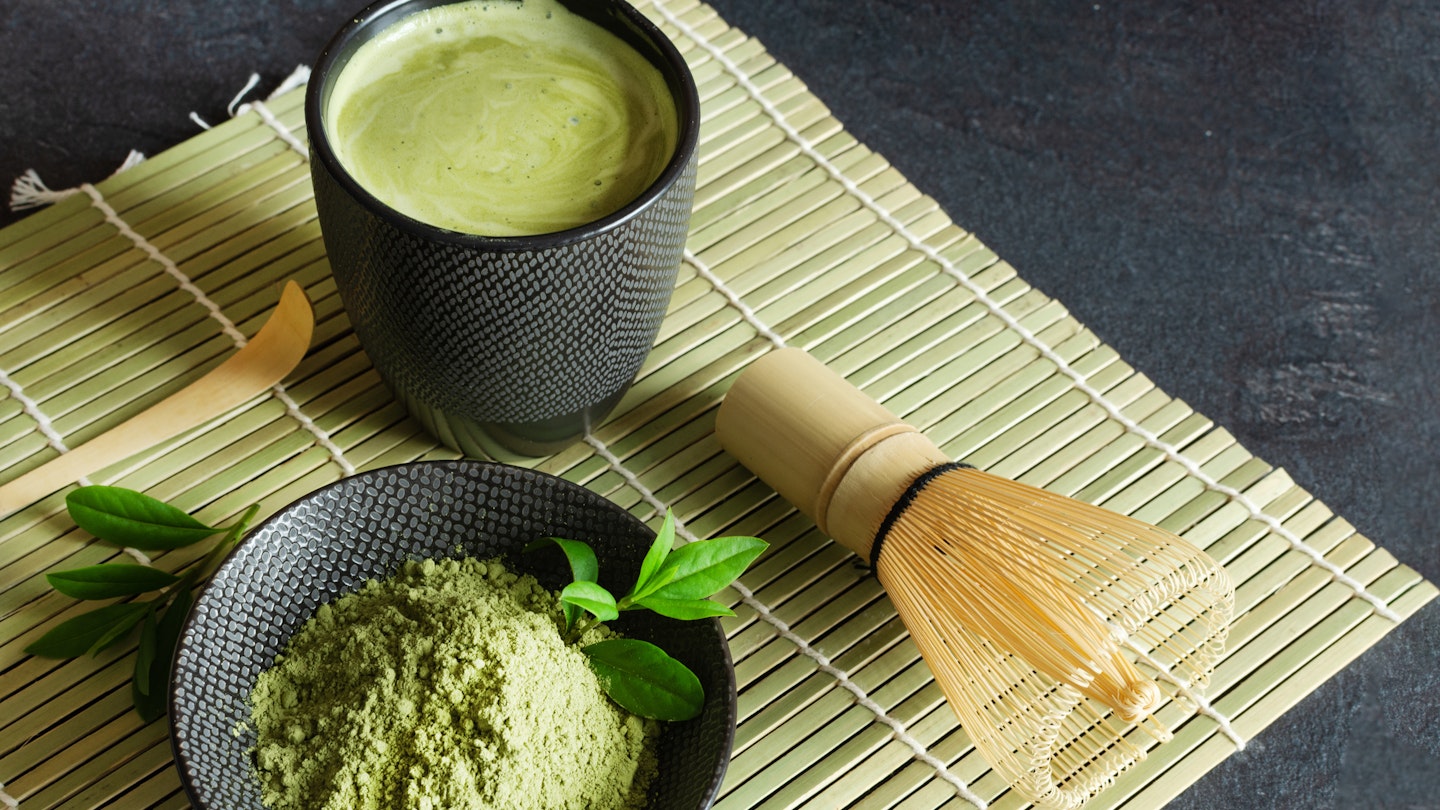 Organic green matcha tea and tea accessories on japanese mat on black background.